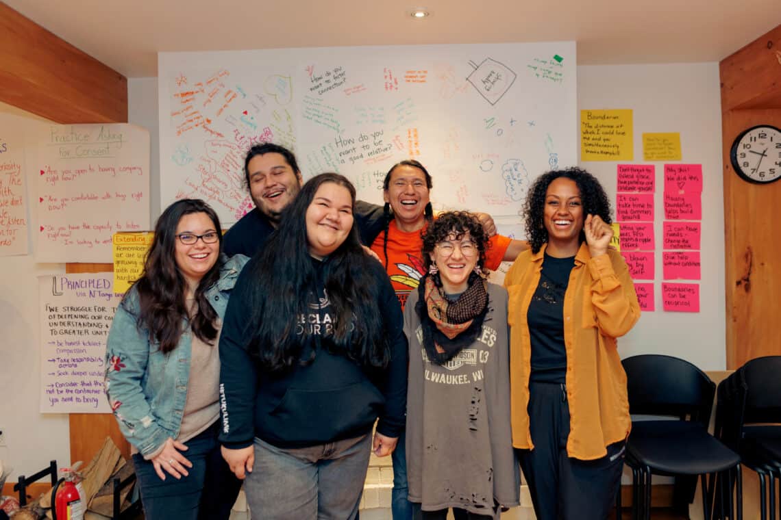 A group of six people smiling in front of a dry-erase board with notes.