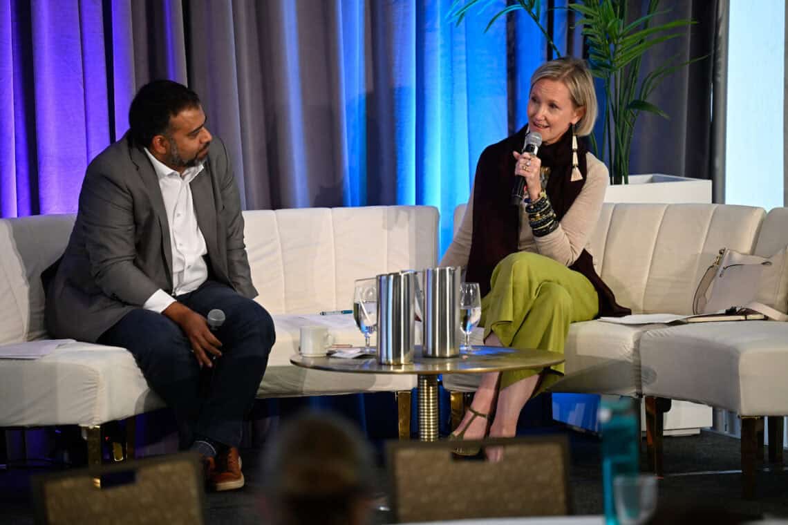 Two people facing one another on a couch. One is speaking with a mic.