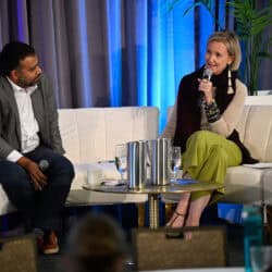 Two people facing one another on a couch. One is speaking with a mic.