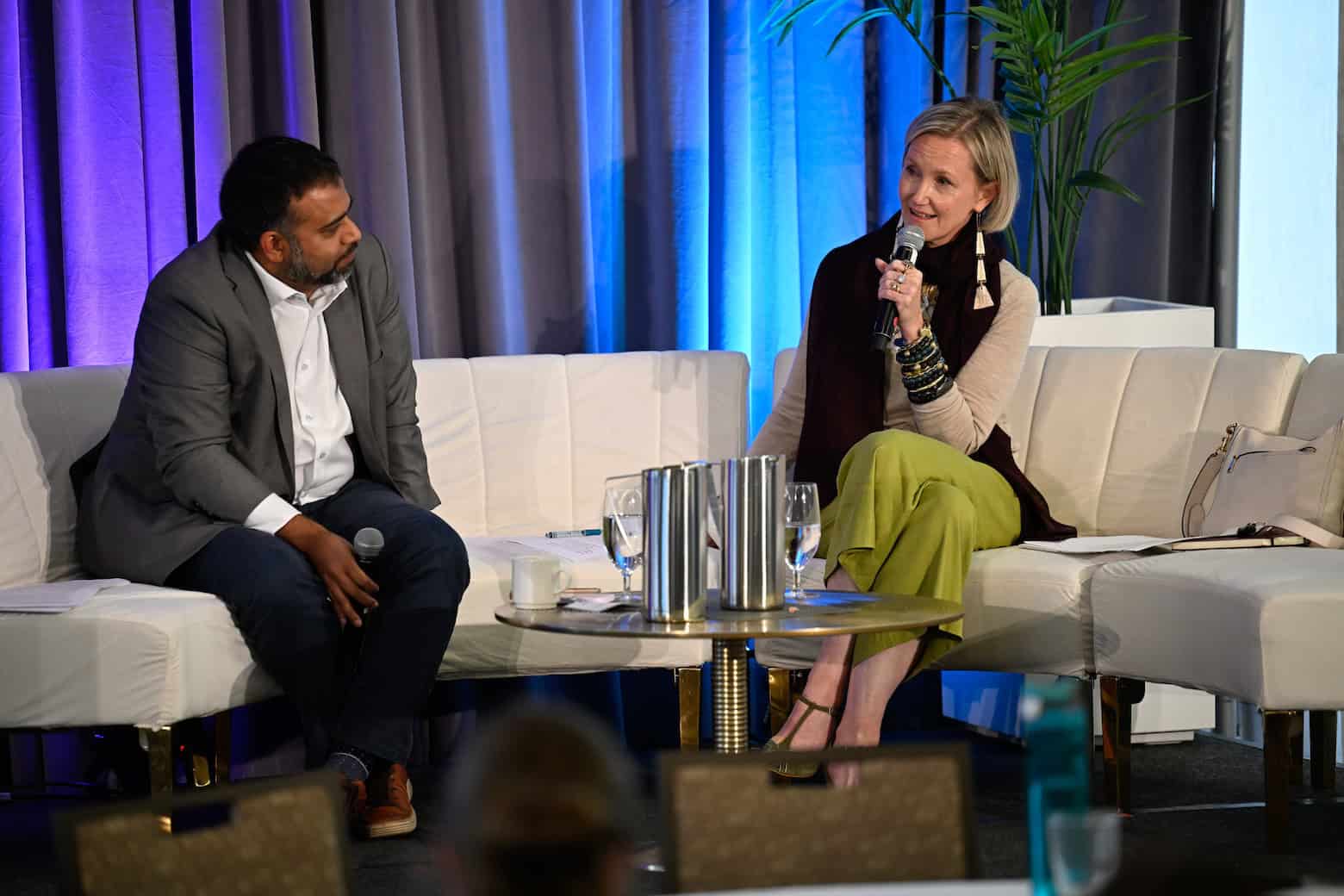 Two people facing one another on a couch. One is speaking with a mic.
