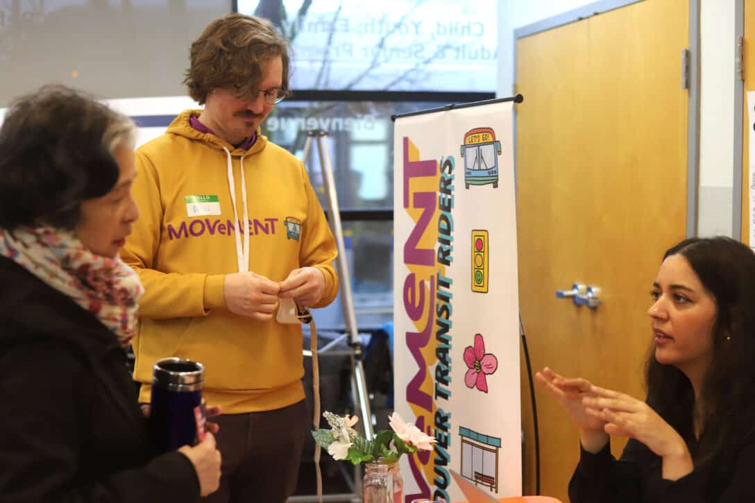 Three people in discussion. One person is wearing a hoodie that says "Movement"