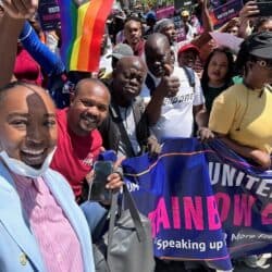 Cheerful people holding a "United for Rainbow Equality" banner outside with a pride flag.