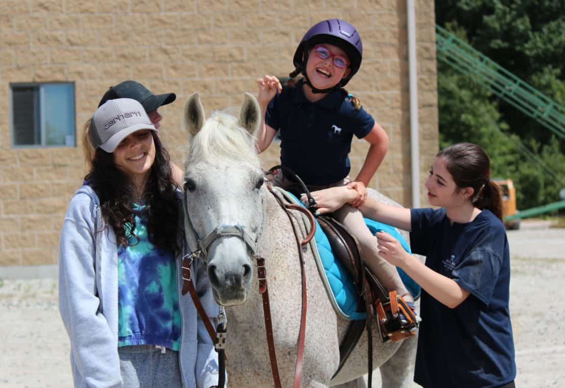 A child on a horse smiling, with three others alongside the horse.