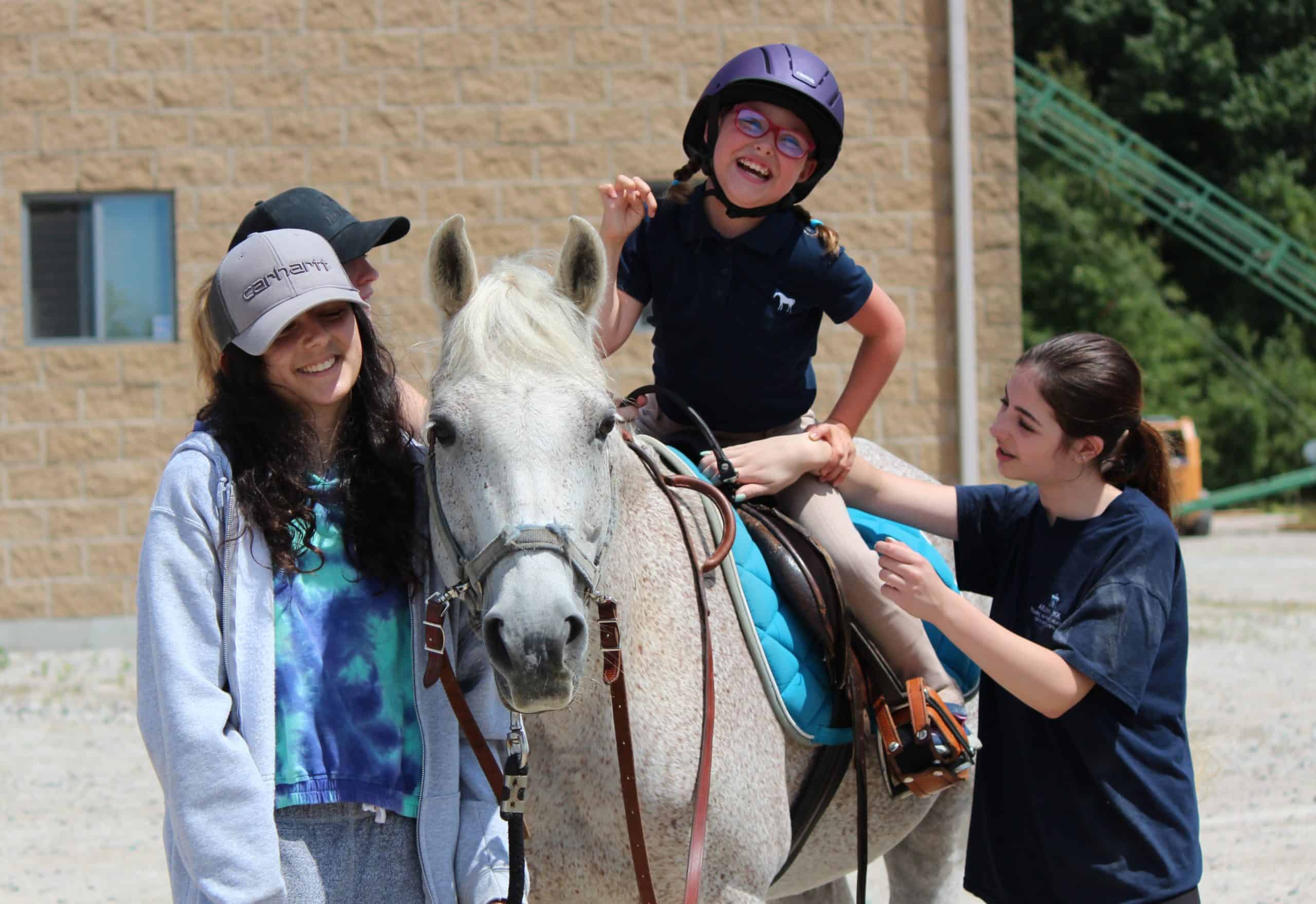 A child on a horse smiling, with three others alongside the horse.