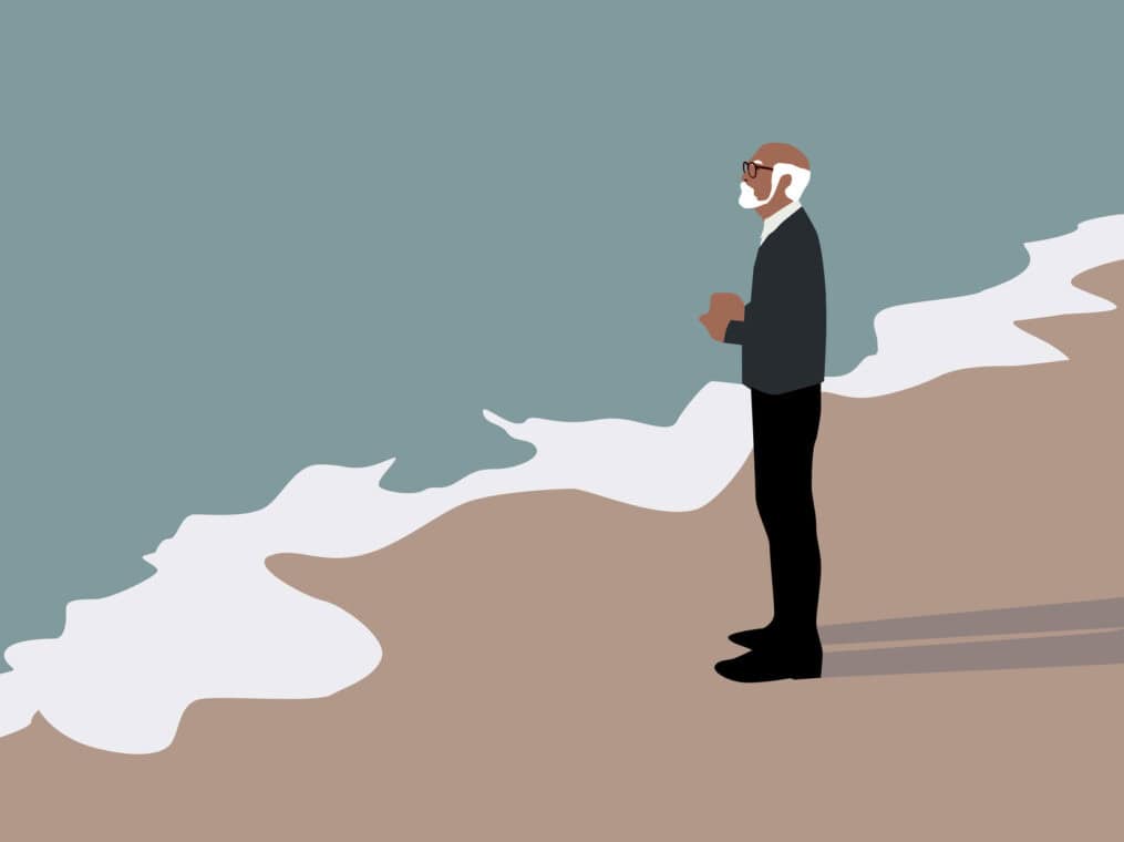 A thoughtful white-haired man stands alone at the seashore.