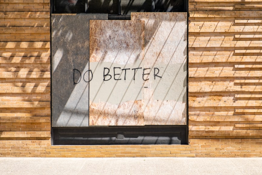 The words Do Better are spray painted on a boarded up window