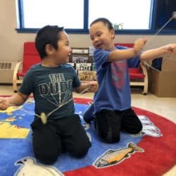 Two children are playing with string toys and smiling.