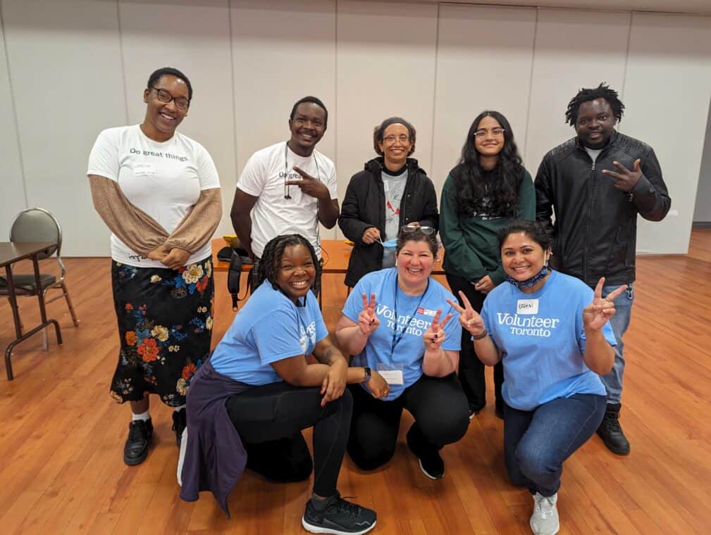 A group of eight people posing for the camera. Three people are wearing "Volunteer Toronto" t-shirts