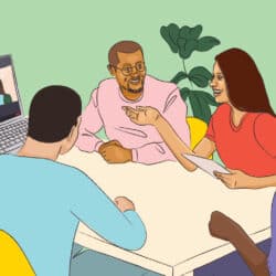 A group of people sitting around a table talking with another person participating on a computer screen.