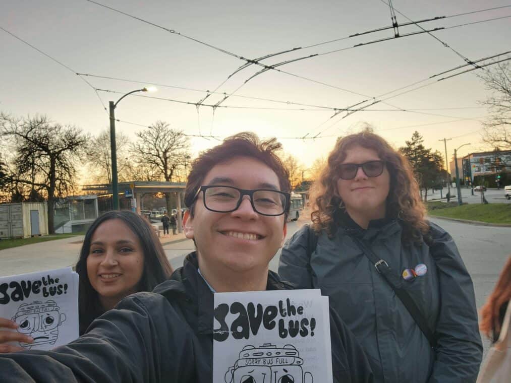 Three people smiling and holding pamphlets that say "save the bus!"