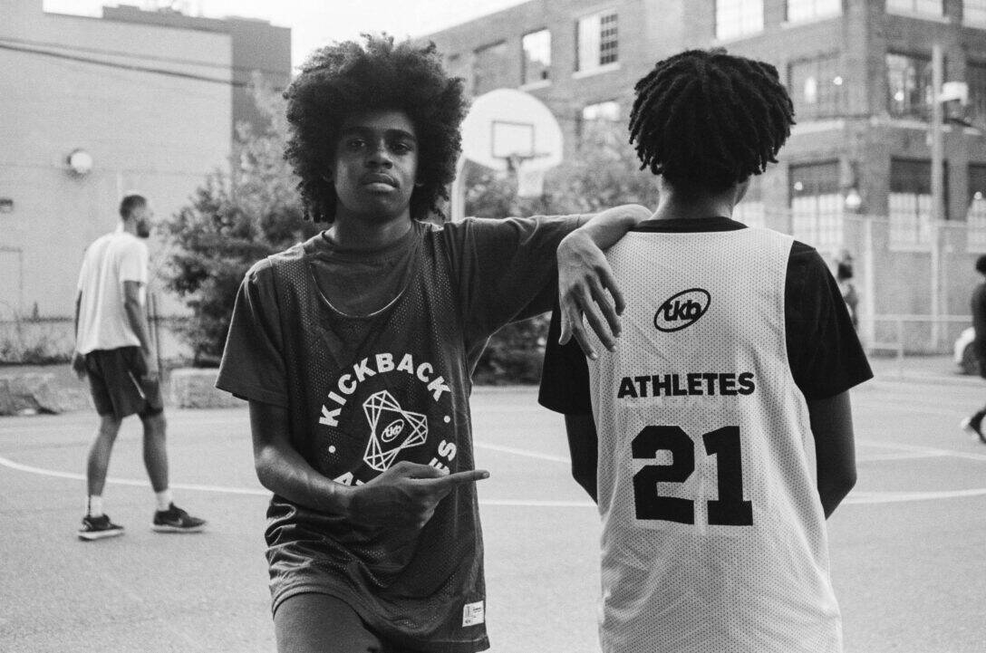 Two young people on a basketball court with jerseys that say "Kickback"