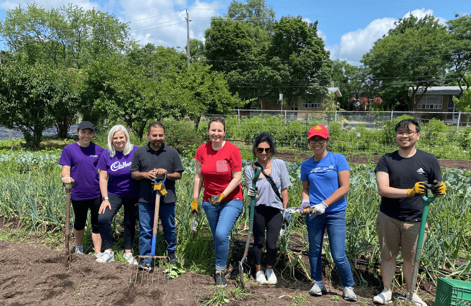 People posing with shovels in front of a garden